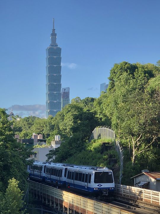Taipei 101 above the treeline, with a Taipei Metro train on the elevated track below